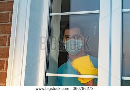 Quarantined Chores. Man In A Medical Mask Cleans Windows During Quarantine. House Cleaning During Qu