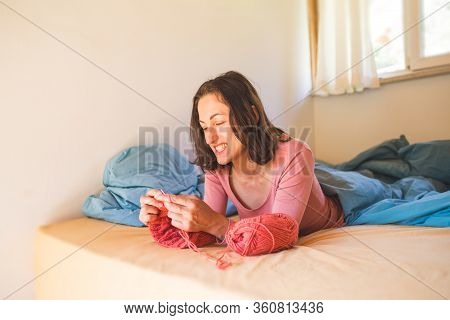 Woman Knits While Lying On The Bed.