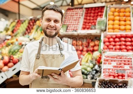 Waist Up Portrait Of Bearded Man Wearing Apron And Smiling At Camera While Standing By Fruit And Veg
