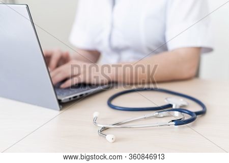 Unrecognizable Female Doctor In Uniform Uses A Laptop. Faceless Medical Worker Writes A Report On Th