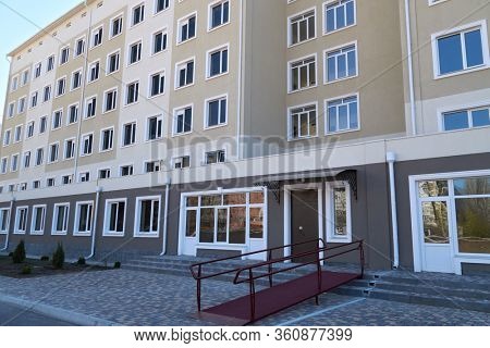 Wheelchair access ramp for entrance of residential multistory building, city street and tiles sidewalk