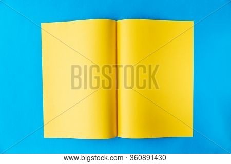 Yellow Sheet Of A3 Paper Folded In The Middle In A Spread On A Blue Background With A Place For Text