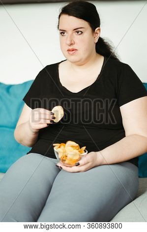 Overeating And Gluttony Concept. Mindless Snacking, Home Sedentary Lifestyle. Obese Woman Sitting On