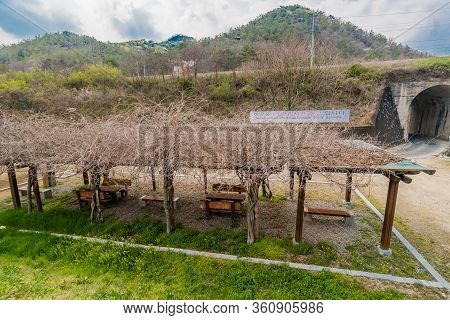 Hwanggan, South Korea; April 10, 2020: Covered Picnic Tables In Front Of Arched Bridge And Sign Of T