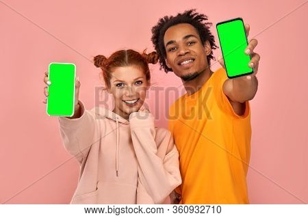Delighted Handsome Black Man And Ginger Woman Points At Mock Up Green Screen Of Smartphone For Your 