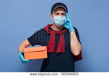 Closeup Portrait Of Deliveryman Standing Against Blue Studio Wall With Finger Near Temple, Guy Forgo
