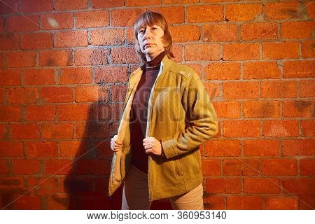 A Middle-aged Woman Poses Showing Clothes Near Red Brick Wall. An Inept Model In An Inept Shoot