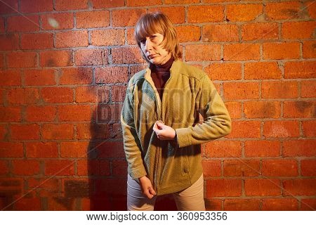 A Middle-aged Woman Poses Showing Clothes Near Red Brick Wall. An Inept Model In An Inept Shoot