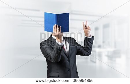 Businessman Covered His Face With Book And Finger Pointing Up. Portrait Of Man In Business Suit Stan