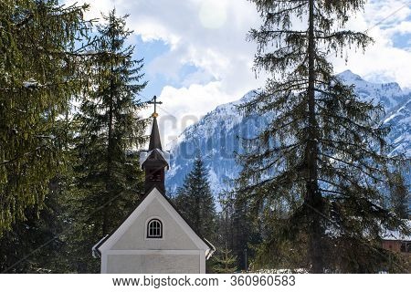 Small Church Enclosed In The Woods And Snow-capped Peaks Of The Dolomites Near The Algo Di Dobbiaco 