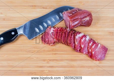 Sliced Air-cured And Smoked Pork Neck, Unsliced Rest Of The Piece And Kitchen Knife On The Bamboo Wo