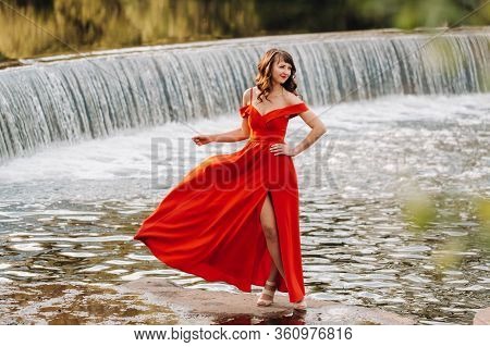 A Young Beautiful Girl With Long Brown Hair, In A Long Red Dress With A Ring Around The Lake