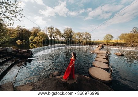 A Young Beautiful Girl With Long Brown Hair, In A Long Red Dress With A Ring Around The Lake.