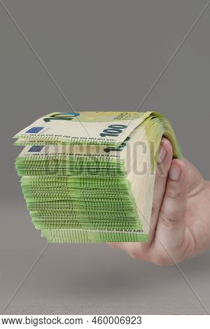 Large Stack Of Euros In Hand. Banknotes Of 100 Euros In A Male Hand On A Uniform Background. A Man H