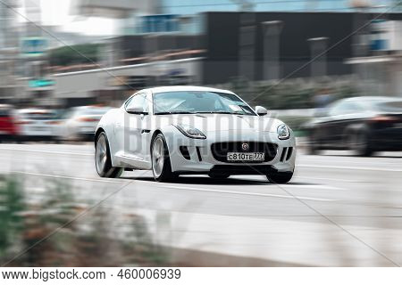 Jaguar F-type S Coupe Driving On The Street In Moscow. White Supercar Moving Fast In Front Of Blurre
