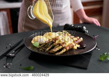 Baked Aspargus Covered With Bacon And Poached Eggs On A Black Ceramic Plate