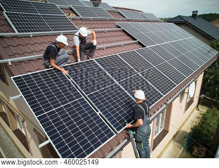 Men Installers Mounting Photovoltaic Solar Moduls On Roof Of House. Engineers In Helmets Installing 