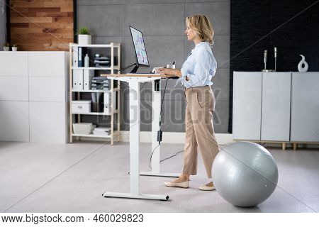 Woman Using Adjustable Height Standing Desk In Office For Good Posture