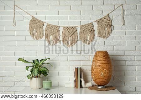 Potted Houseplant, Decor Elements And Books On White Table Near Brick Wall With Stylish Macrame