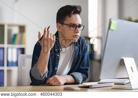 Confused Male Office Employee Sitting At Wokplace And Looking At Computer Screen