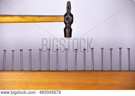 A Few Nails Driven Into The Board And A Small Hammer On A Light Background