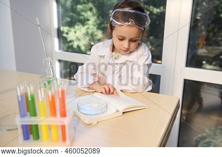 View From Above Of A Smart School Child, Little Caucasian Girl In Protective Lab Wear Reading Chemis