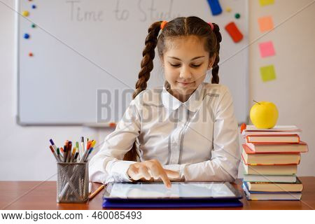 Little Smiling Girl Working On The Tablet Computer In The Classroom. Modern Technologies In Educatio
