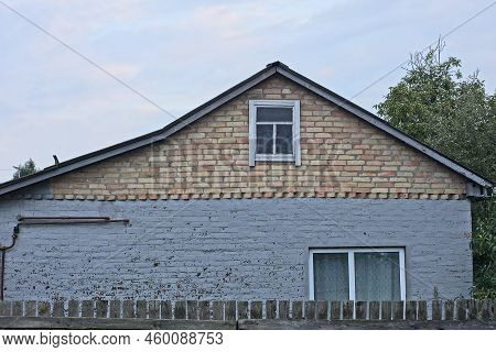 Brown Attic With A Small Window Of A Gray Rural House On The Street Against The Sky