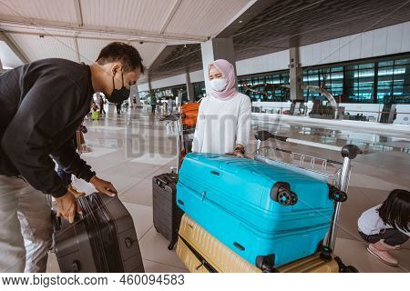 Muslim Woman And Husband Carrying A Lugage In The Airport