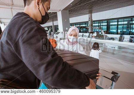 Muslim Woman And Husband Carrying A Lugage In The Airport