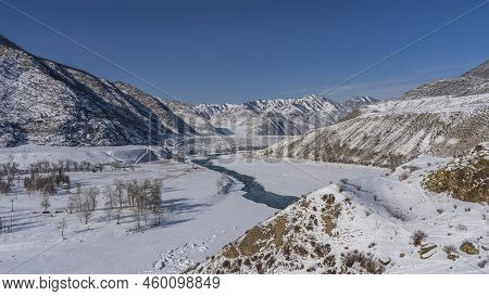 The Ice-free Turquoise River Winds Between The Icy Shores. Bare Trees In A Snowy Valley. Picturesque