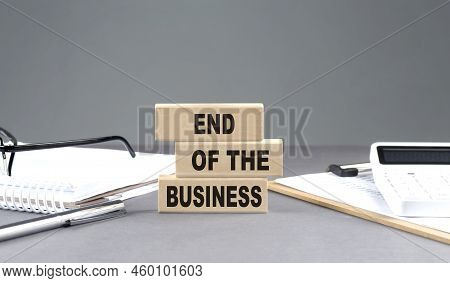 End Of The Business Text On Wooden Block With Notebook,chart And Calculator, Grey Background