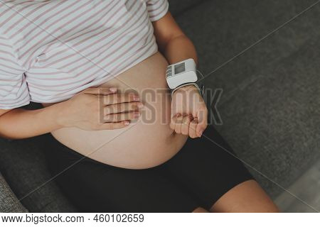 A Pregnant Woman Sits On The Couch And Measures Her Blood Pressure, Her Face Is Not Visible