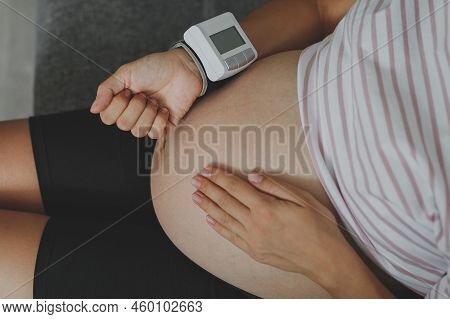 A Pregnant Woman Sits On The Couch And Measures Her Blood Pressure, Her Face Is Not Visible