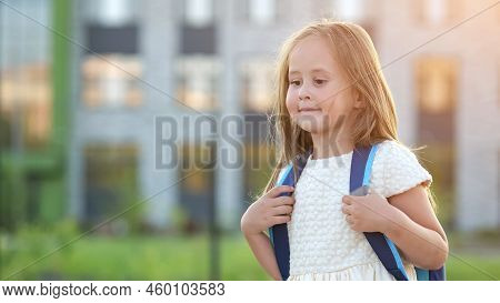 Happy Girl Goes To School In Preparatory Form. Excited Preschooler Girl With Backpack Walks Near Spo