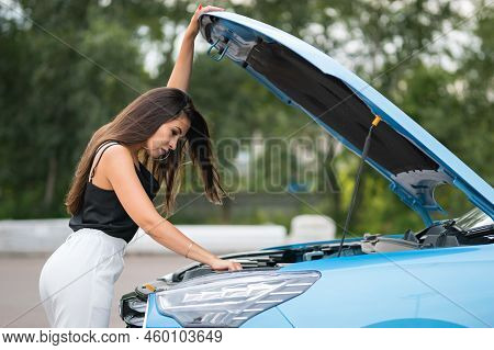 Elegant Black-haired Businesswoman Tries To Repair Blue Car On Parking Lot. Woman Driver Has Motivat