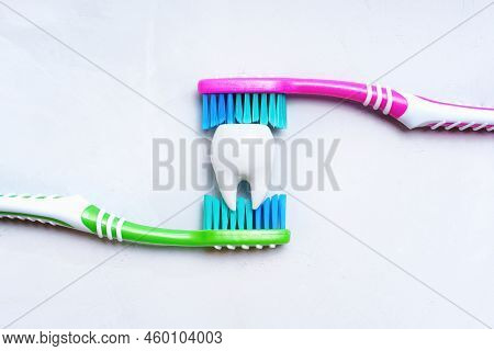 Large White Tooth Between Two Colorful Toothbrushes Isolated On A Neutral Background. Teeth Brushing