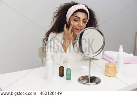 Close Up Portrait Of Enjoyed Tanned Pretty Curly Latin Lady Admiring Herself In Mirror Use Facial Cr