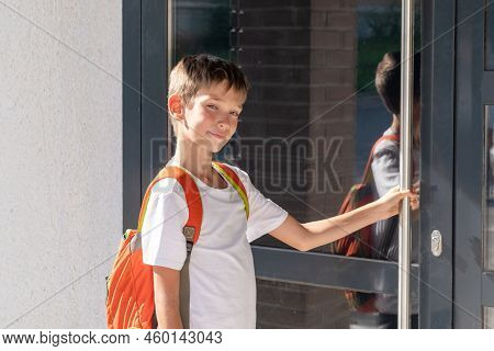 Cute Boy Student With A School Backpack Opens The Door Of The House. A Child Returning Home After Sc