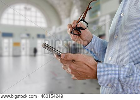Male Tourist With Glasses Checking E-ticket On Mobile Phone In Public Transportation Terminal