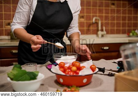 Cropped View. Details: Hands Of A Housewife In Black Chefs Apron Holding Wooden Teaspoon With Sugar 