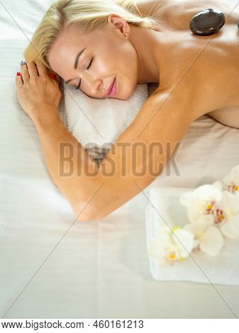 Beautiful Young Woman With Eyes Closed Receiving Hot Stone Massage At Salon Spa