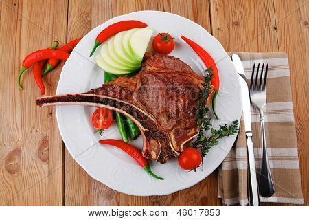 cibo di carne: arrosto nervatura sul piatto bianco con pepe timo e pomodoro sul tavolo di legno