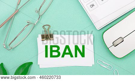 On A Light Green Background There Is A White Calculator, A Computer Mouse, Green Leaves Of A Plant, 