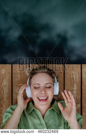 Reaxed Woman With Headphones Listening To Music And Singing For Herself, Lying On A Pier By Natural 