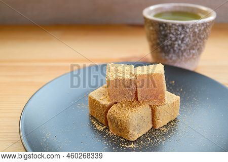 Plate Of Warabimochi, A Japanese Traditional Confection With Blurry Hot Matcha Green Tea In Backdrop