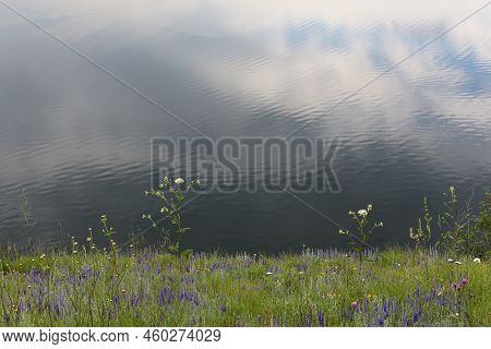 A Green Bank Of The Lake. Sky And Clouds Reflected In Water. A Large Calm River In Summer.