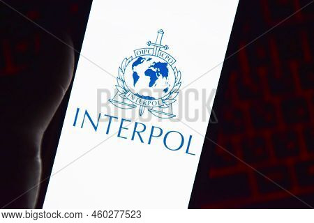 Person Holding Smartphone With Interpol Logo Displayed On Screen.