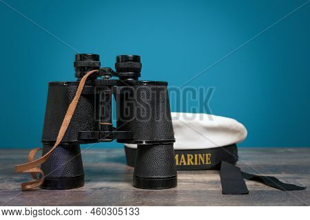 Old Ship\'s Binoculars And Peakless Cap On A Turquoise Background On A Textured Wooden Table