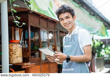Male Chicken Noodle Seller Wearing Apron Smiling Using Digital Tablet